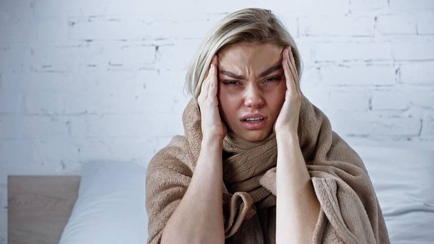 sick woman looking at camera while suffering from migraine in bedroom - Photo, image