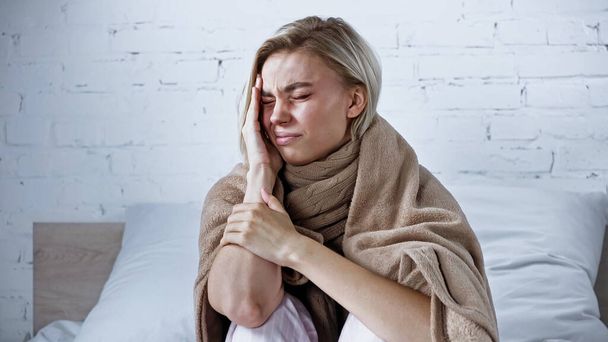 femme malade, enveloppée dans une couverture chaude, souffrant de maux de tête dans la chambre - Photo, image