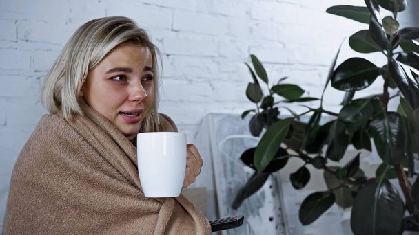 donna malata che tiene una tazza di tè mentre guarda un film in camera da letto - Foto, immagini