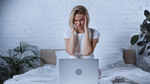 młody freelancer cierpiący na migrenę w pobliżu laptopa w sypialni - Zdjęcie, obraz
