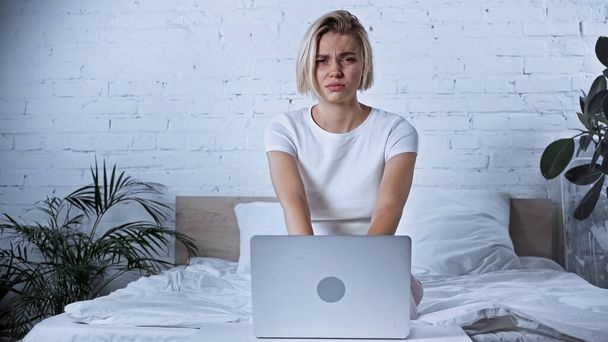 sick freelancer looking at camera near laptop in bedroom - Photo, Image