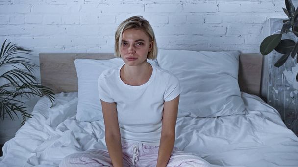 upset diseased woman in pajamas looking at camera while sitting in bedroom  - Фото, зображення
