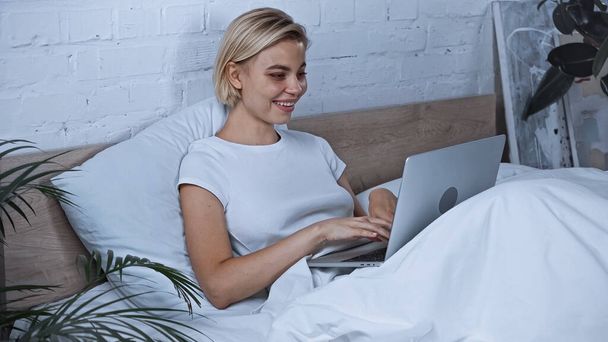 cheerful blogger typing on laptop in bedroom - Φωτογραφία, εικόνα
