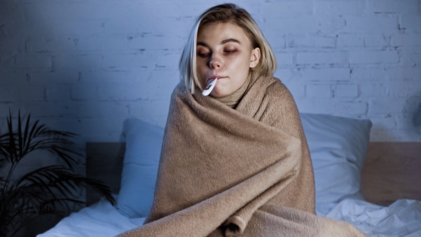 ill woman, wrapped in warm blanket, measuring temperature in bedroom - Foto, Imagem