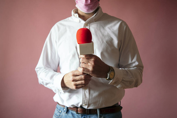 Δημοσιογράφος φορώντας μάσκα με μικρόφωνο στέκεται με ροζ φόντο - Φωτογραφία, εικόνα