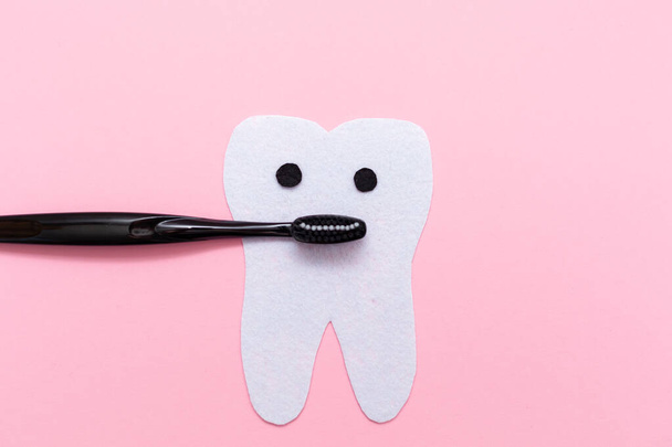 Μια μαύρη οδοντόβουρτσα που συμβολίζει ένα στόμα, με ένα δόντι κομμένο από τσόχα. Επίπεδη. Αντιγραφή χώρου. Η έννοια της στοματικής υγιεινής. - Φωτογραφία, εικόνα