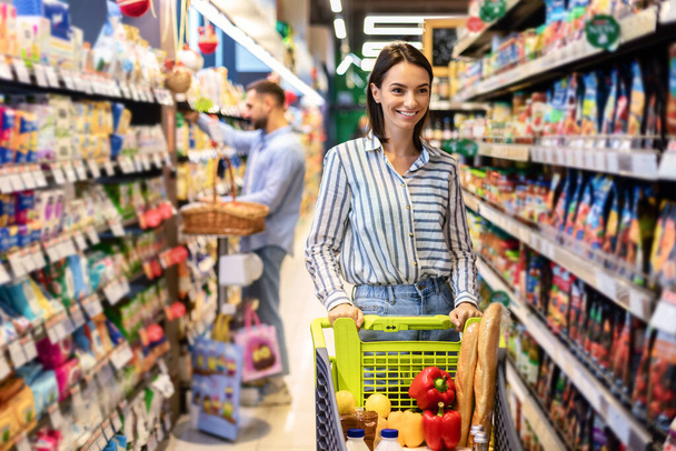 Lässige Frau kauft mit Einkaufswagen im Supermarkt ein - Foto, Bild