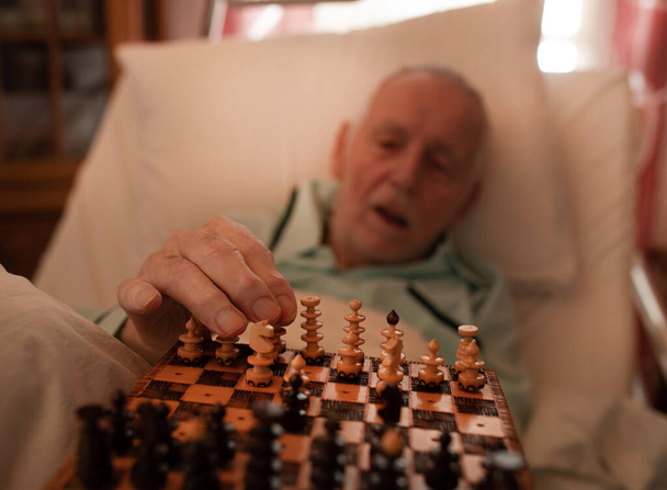 Großaufnahme der Hand eines älteren Mannes, der im Bett Schach spielt - Foto, Bild