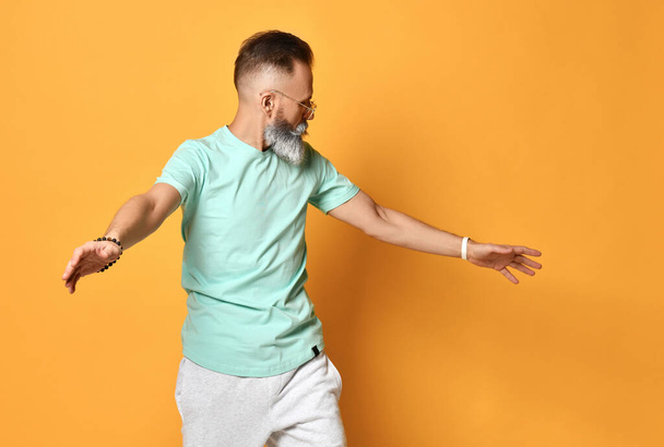 Stylish trendy gray-haired hipster guy dancing and having fun on bright orange background. - 写真・画像