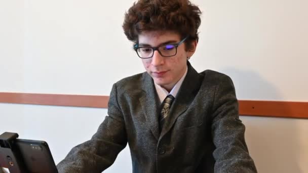 Egy fiatal kaukázusi fiú újságírónak öltözött, és egy távoli interjúra készül az okostelefonjával, amit egy kis állvány támogat. A vállalkozó szellemű fiatal újságíró fogalma. - Felvétel, videó