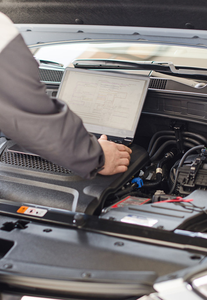 Mechanic with laptop diagnoses car in workshop. - Valokuva, kuva