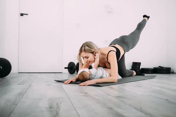 Uma jovem mãe europeia com sua filhinha no chão está fazendo fitness e alongamento. Fazer esportes em casa. Lugar para texto. - Foto, Imagem