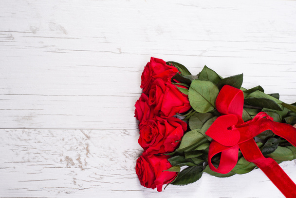 Ramo de rosas rojas con corazón decorativo y cinta en el fondo de madera blanca. Fondo de San Valentín. Tarjeta de felicitación plantilla de flores. Banner de felicitación.. - Foto, Imagen