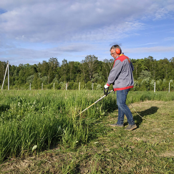 Homem corta a grama com um aparador, grama alta em um prado, feito à mão no garden.new - Foto, Imagem