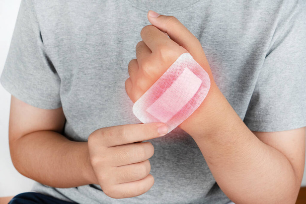 Boy putting adhesive bandage, plaster or band-aid on a cut hand. isolated on white. Bandage plaster closed wound on boy hand against white background. - Photo, Image