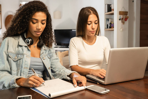 İki genç çağın kadın girişimcisi evde dizüstü bilgisayar ve akıllı telefonla çalışıyor oturma odasında notlar yazıyor. Yeni Normal İnternet işleri mobil bağlantıları olan her yerde çalışmanızı sağlar - Fotoğraf, Görsel