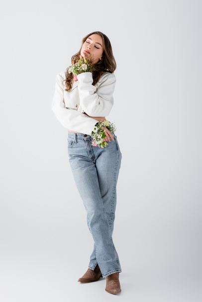 Brunette woman with flowers in sleeves of jacket standing with closed eyes on grey background  - Fotoğraf, Görsel