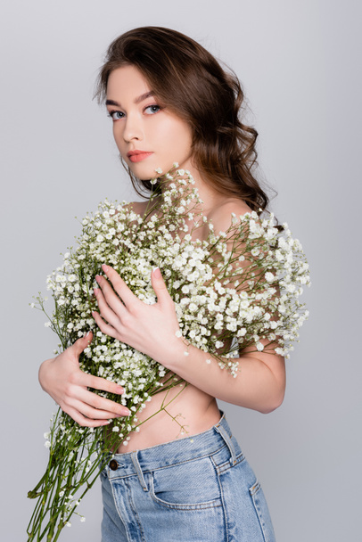 Shirtless brunette woman with small white flowers looking at camera isolated on grey - Foto, Imagem