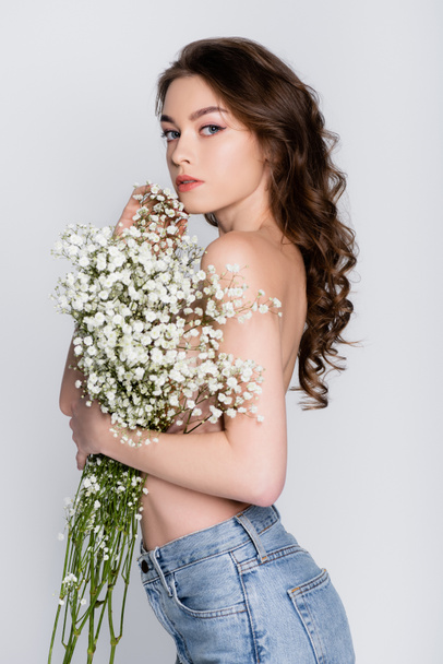 Shirtless woman in jeans holding small white flowers isolated on grey  - Foto, afbeelding