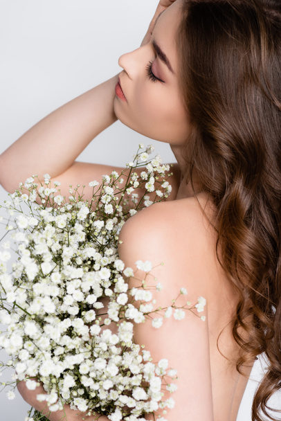brunetka bez koszuli kobieta gospodarstwa białe kwiaty na zamazanym pierwszym planie odizolowany na szary  - Zdjęcie, obraz