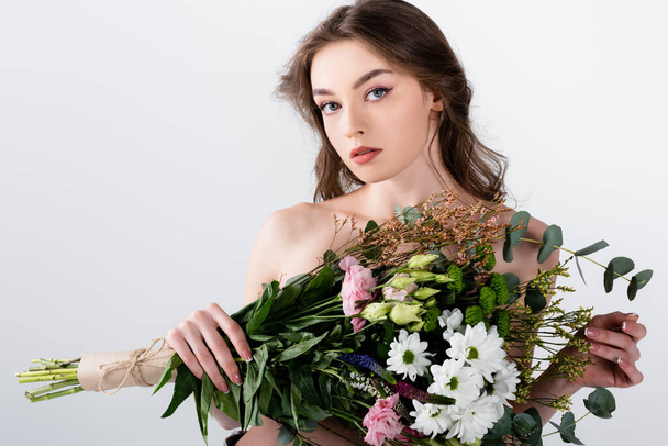 Woman with naked shoulders holding flowers and looking at camera isolated on grey  - Foto, imagen