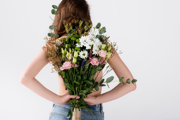Back view of model in jeans holding flowers isolated on grey  - Photo, Image