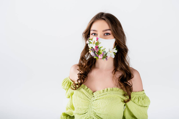 Brunette woman in medical mask with flowers and green blouse looking at camera isolated on grey  - Photo, Image