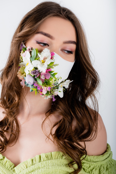 Woman in medical mask with flowers and green blouse looking away isolated on grey  - Foto, Imagen