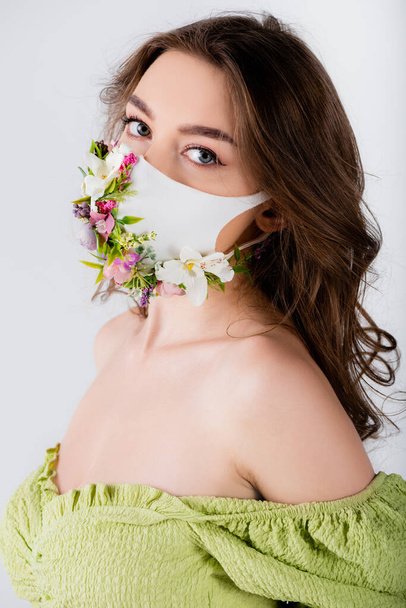 Brunette woman in trendy blouse and medical mask with flowers looking at camera isolated on grey  - Valokuva, kuva