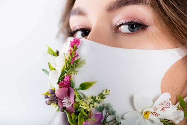 Mulher em máscara médica com flores olhando para câmera isolada em branco - Foto, Imagem