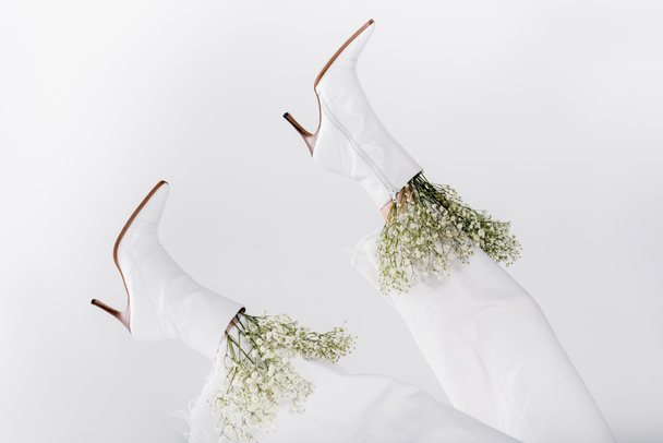 Częściowy widok małych białych kwiatów w butach kobiety odizolowanych na szarości  - Zdjęcie, obraz