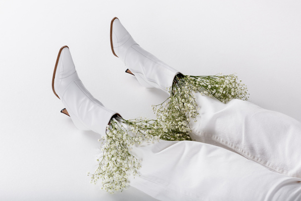 Cropped view of legs of woman in white shoes and pants with flowers on grey background - Photo, image