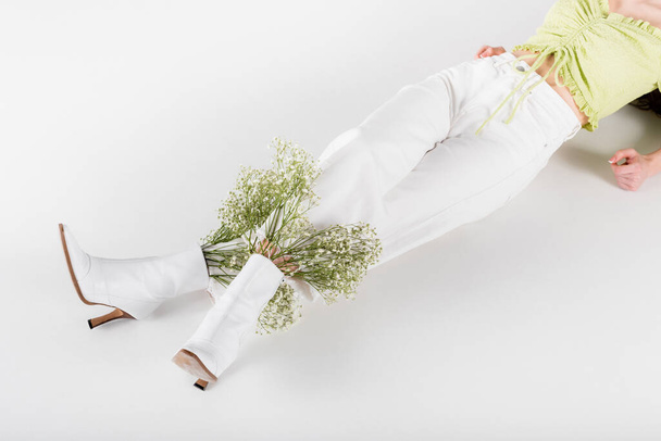 Oříznutý pohled na stylové ženy s květinami v obuvi ležící na šedém pozadí - Fotografie, Obrázek