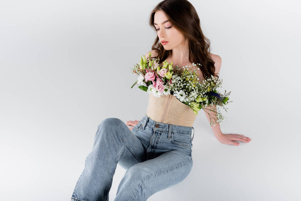 Woman in jeans and blouse with flowers sitting isolated on grey  - Fotoğraf, Görsel