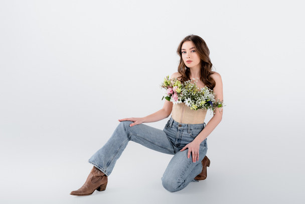 Brunette woman in brown shoes, jeans and flowers in blouse on grey background - Photo, Image