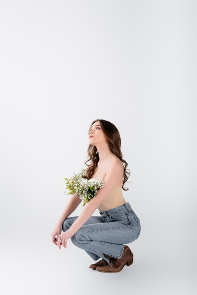 Stylowa kobieta z kwiatami w bluzce patrząc w górę na szarym tle - Zdjęcie, obraz