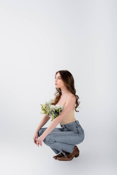 Young woman with naked shoulders and flowers in blouse looking away on grey background - 写真・画像
