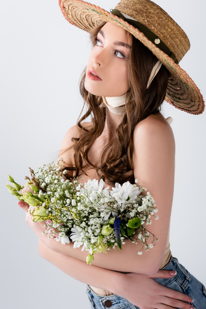 Young woman in stylish straw hat holding flowers isolated on grey  - Φωτογραφία, εικόνα