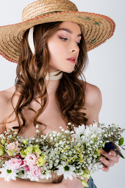 Jeune modèle en chapeau de soleil tenant des fleurs isolées sur gris  - Photo, image
