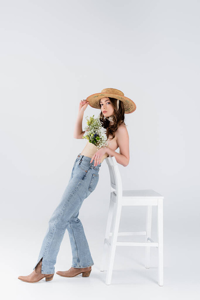 Trendy model with flowers in blouse standing near chair on grey background  - Fotografie, Obrázek