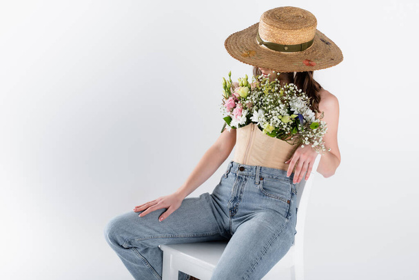 Kobieta z kwiatami w bluzce i kapelusz słoneczny siedzi na białym krześle odizolowany na szaro  - Zdjęcie, obraz