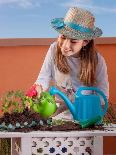 Gardener girl watering various plants for the garden with a sprayer on a table and a blue watering can in the composition. - Photo, Image
