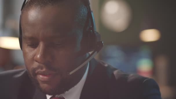 Στιγμιαία φωτογραφία Αφρο-Αμερικανού επιχειρηματία με ακουστικά που μιλάει στο διαδίκτυο κατά τη διάρκεια της εργάσιμης ημέρας στο γραφείο - Πλάνα, βίντεο