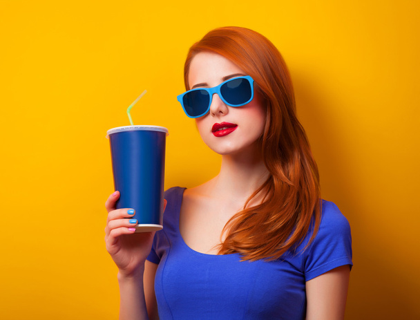 Redhead girl with drink and sunglasses on yellow background - Photo, Image