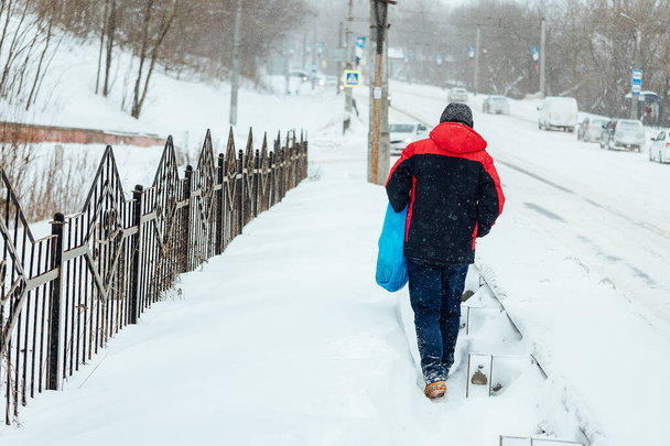 mies, jolla on vaikeuksia kävelee syvässä lumessa, lumi ajelehtii jalkakäytävällä rankan lumisateen jälkeen. yleishyödyllisten laitosten heikko toiminta talvella - Valokuva, kuva