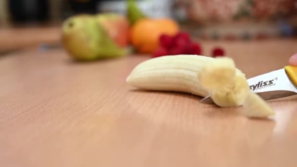 SLOW MOTION slider shot obranego banana siekany na powierzchni roboczej kuchni. Nieostre owoce w tle. - Materiał filmowy, wideo