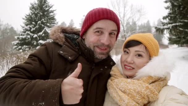 Mittlere Nahaufnahme Handheld POV der schönen asiatischen Freundin und schönen kaukasischen Freund trägt warme Kleidung, zeigt Zungen, macht lustige Gesichter, lächelt und schaut in die Kamera - Filmmaterial, Video
