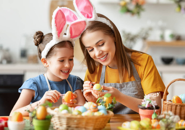 З Великоднем! сім'я: мати і дочка з вухами заєць готується до відпустки, фарбує яйця в затишній кухні вдома
 - Фото, зображення