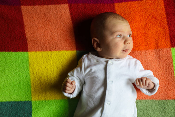Little Caucasian Baby boy 2-3 meses de edad vista lateral del retrato en una manta colorida - Foto, Imagen