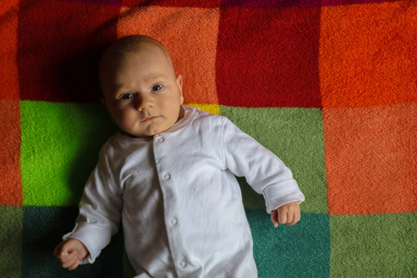 Μικρό Καυκάσιο αγοράκι ηλικίας 2-3 μηνών με πλαϊνή όψη πορτραίτου σε πολύχρωμη κουβέρτα - Φωτογραφία, εικόνα